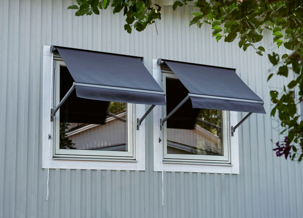 Zwei graue Fenstermarkisen 97x70 cm sind an einer hellgrauen Paneelwand über zwei Fenstern montiert.