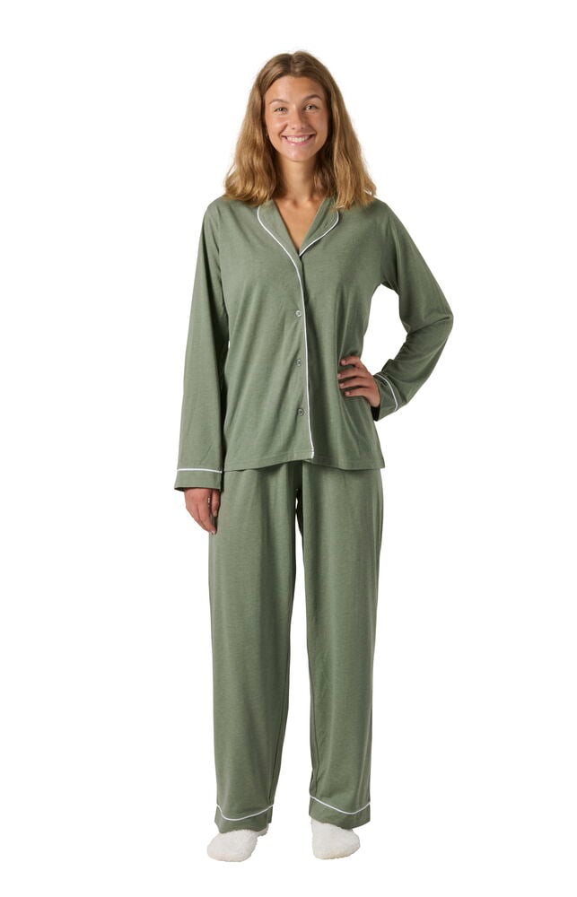 Kvinna bär ett grönt Pyjamas Laura set med vit passpoal på topp och byxor, och vita tofflor.