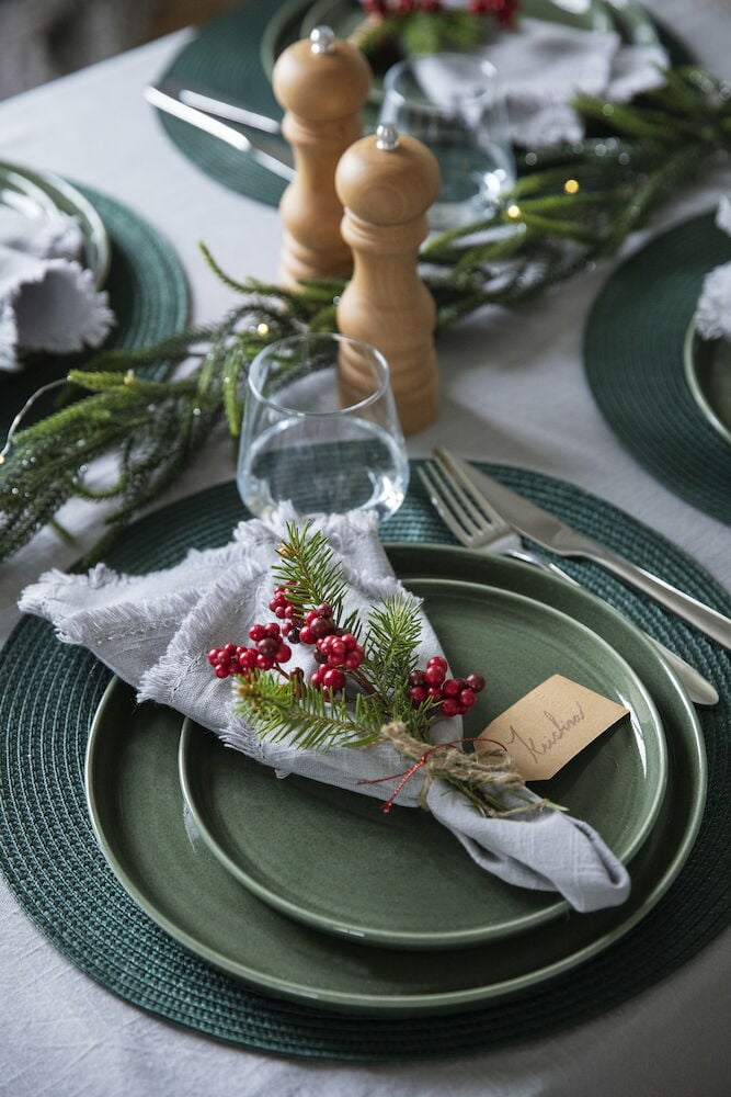 Hellgraue Decke mit Fransen unter weihnachtlich dekoriertem Tischgedeck.