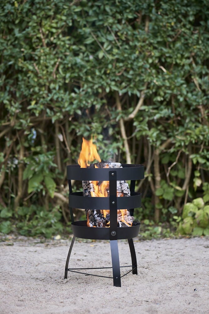 Svart eldkorg med ved och brinnande eld utomhus.