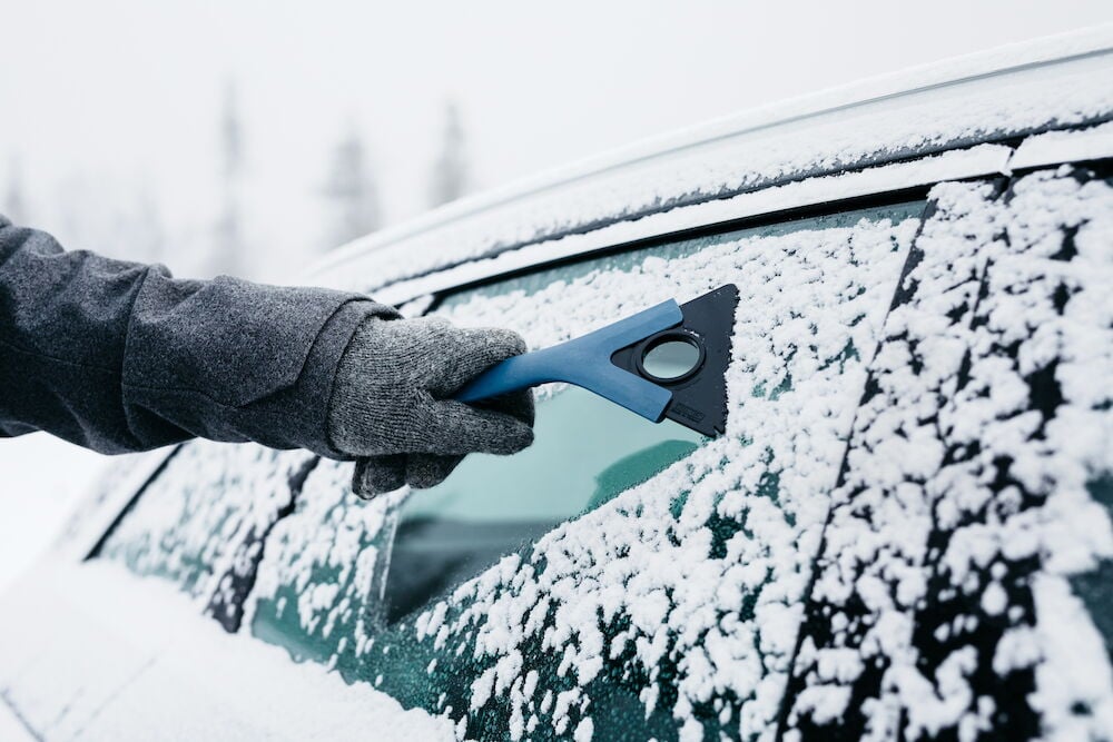 Hand som skrapar is från bilruta med isskrapa.