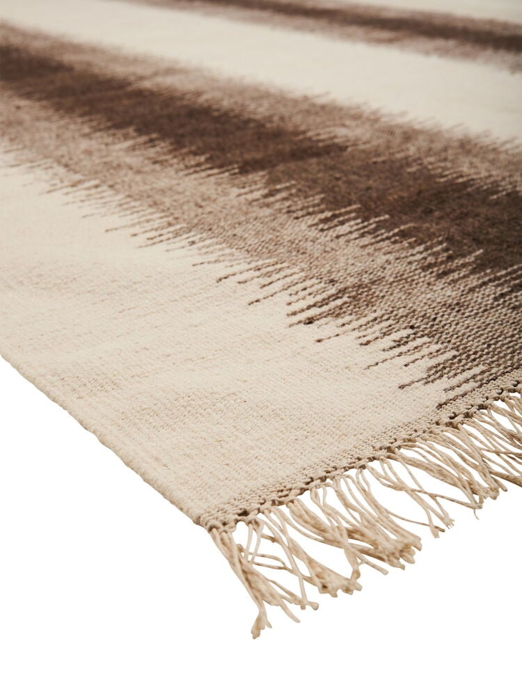 Ruskea käsinkudottu villamatto, jossa on hapsut ja kuvioita.