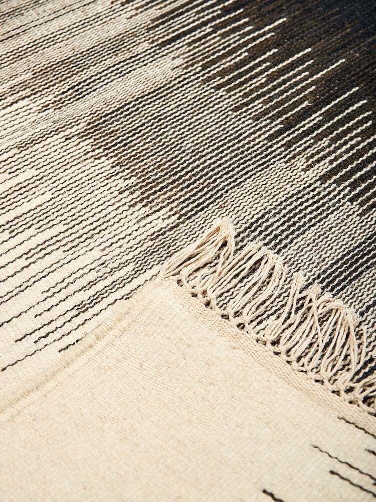 Käsinkudottu villamatto mustavalkoisella designilla ja hapsuilla.