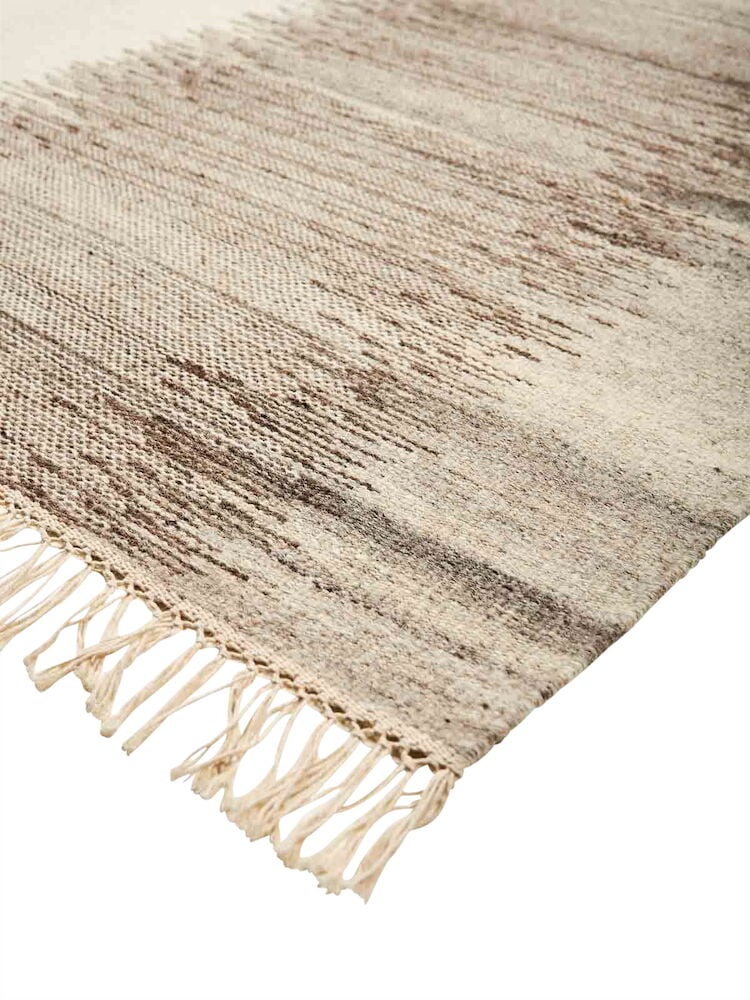 Käsinkudottu beige kelim-matto hapsuilla.