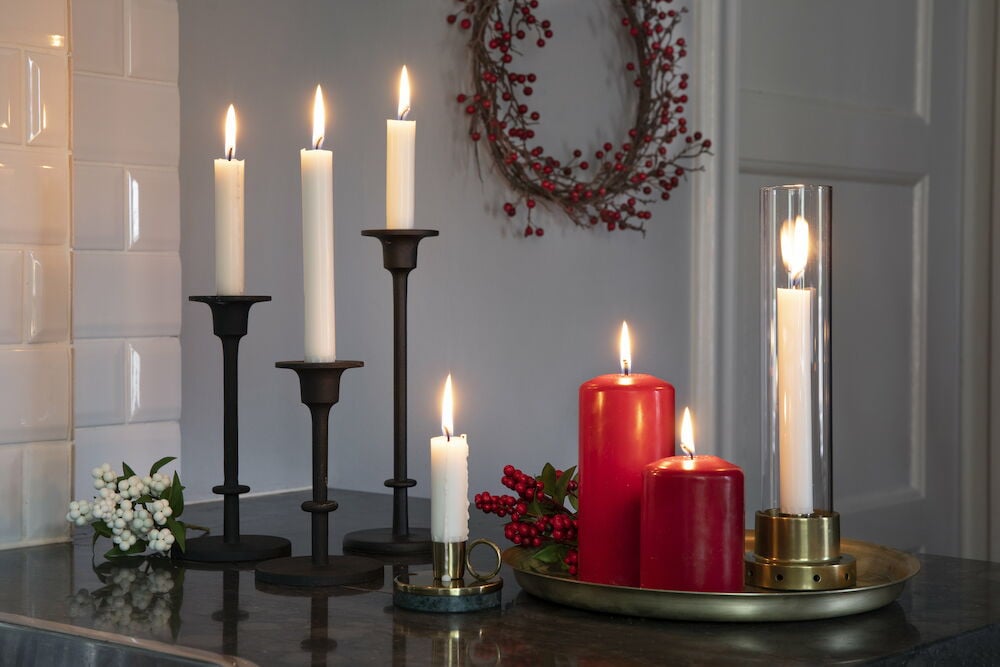 Fyra vita långa stearinljus i svarta ljusstakar.