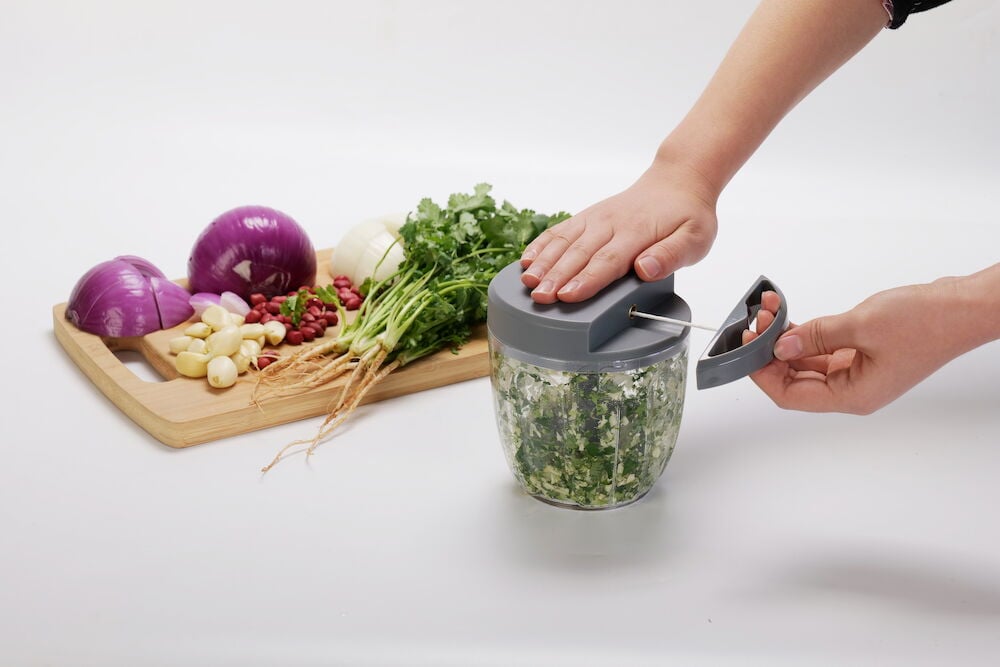 Manuelle Minihacker hackt Gemüse auf einem Schneidebrett.