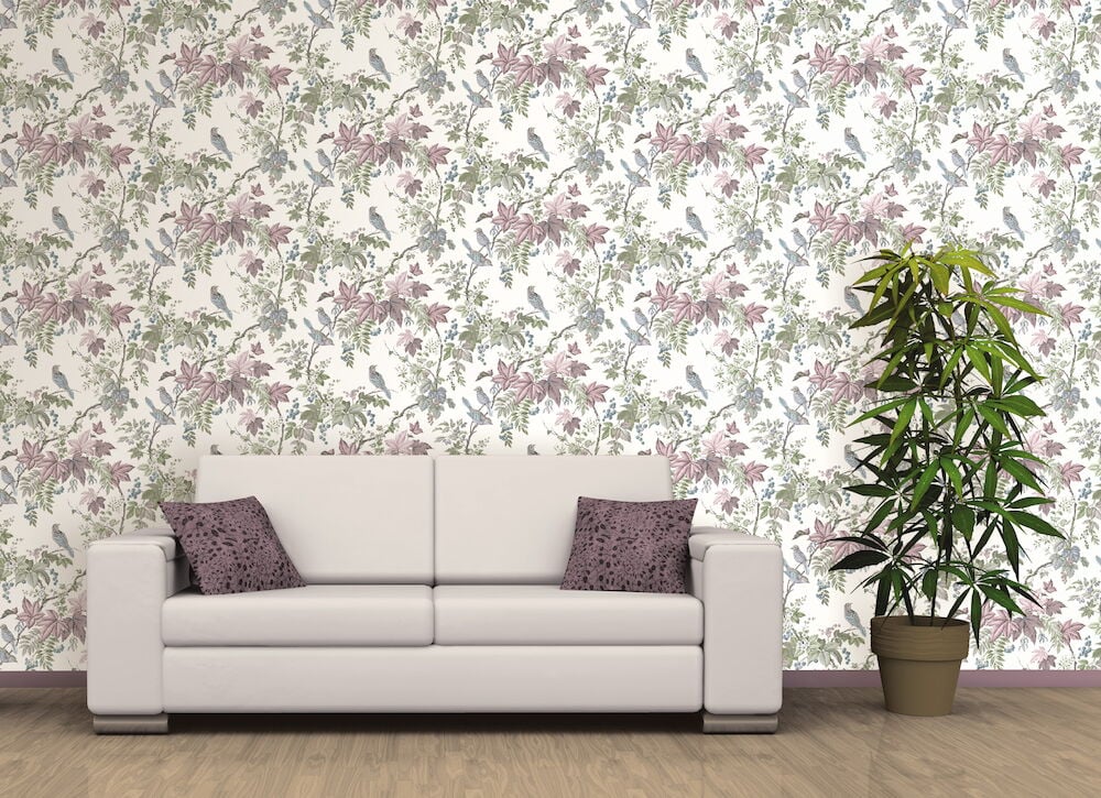 Vaalea sohva kukallisen pastellivärisen tapetin ja huonekasvin edessä.