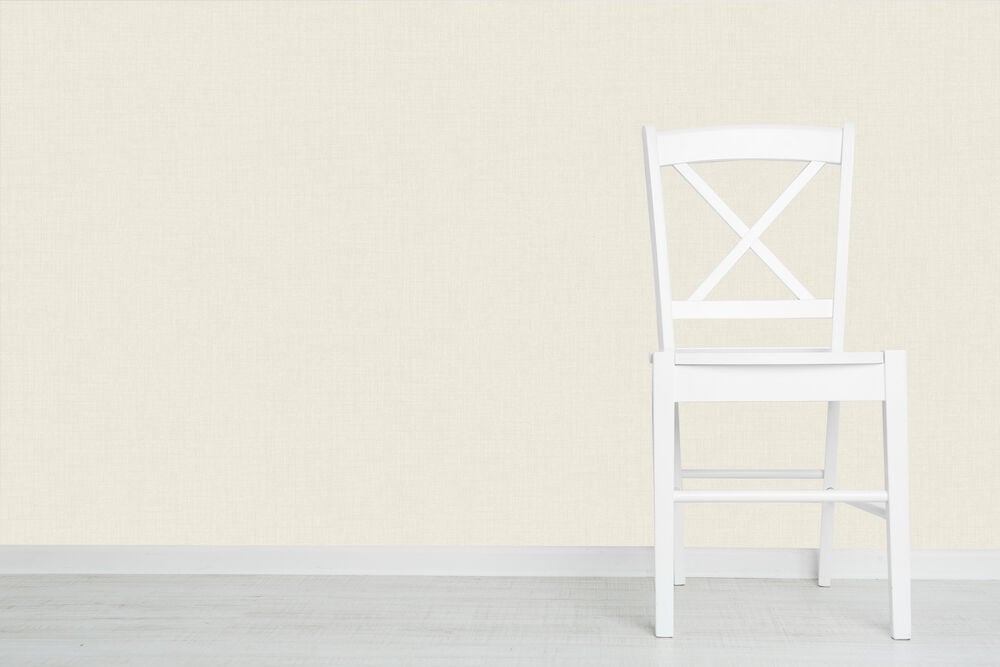 Beigeen värinen tapetti, jossa on rakenne, valkoisen tuolin takana.