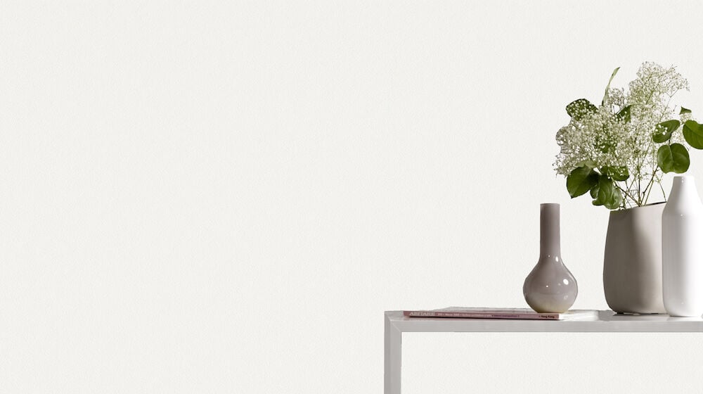 Vit slät tapet bakom bord med vaser och växt.
