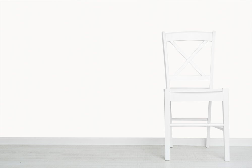 Vit vägg med enfärgad tapet och vit stol.