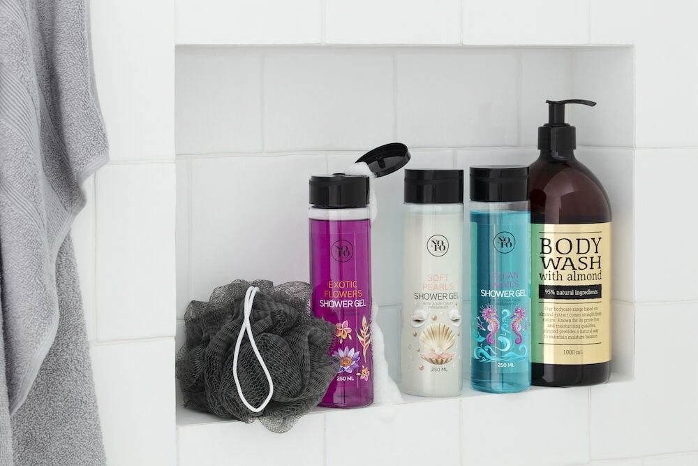 Vier Duschgels und ein schwarzer Duschschwamm in der Dusche.