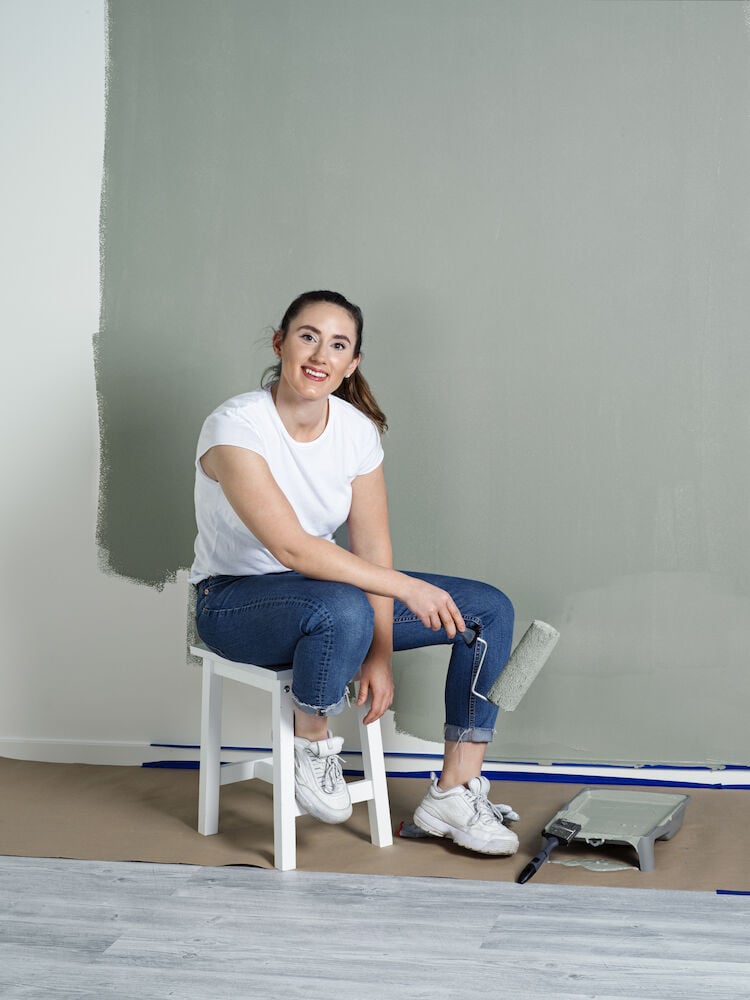 Kvinna målar vägg grön med roller inomhus.