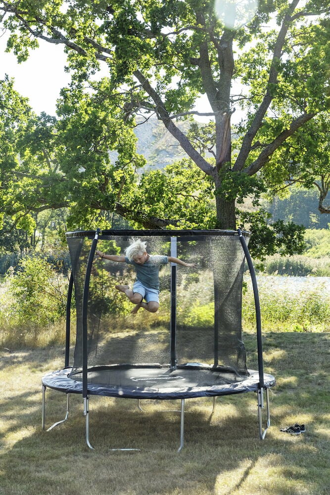 Barn hopper på trampoline med sikkerhetsnett utendørs.
