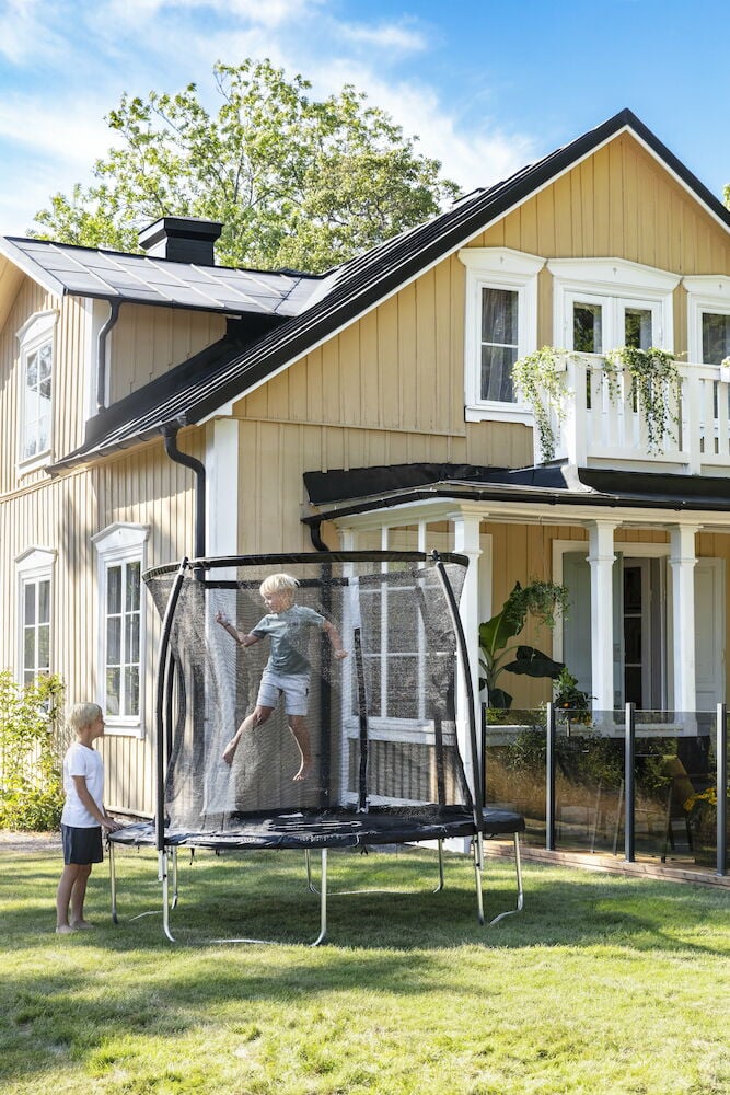 Trampoline med sikkerhetsnett utendørs foran gul villa.