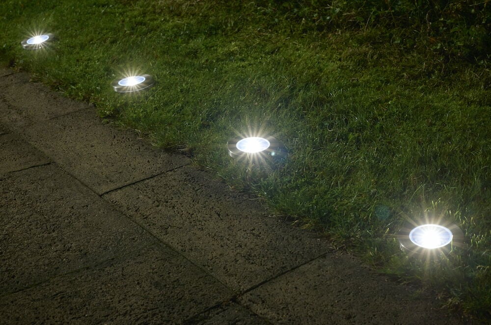 Fem runde solcellebelysninger lyser ved gangsti på gressplen.