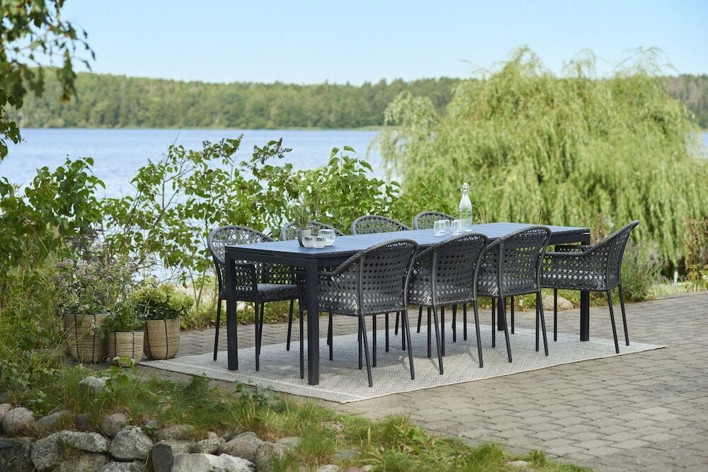 Musta ulkotuolit ruokapöydän ympärillä järven ja vehreyden äärellä.