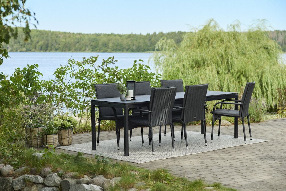 Svarta utomhusdyna på stolar runt matbord utomhus.
