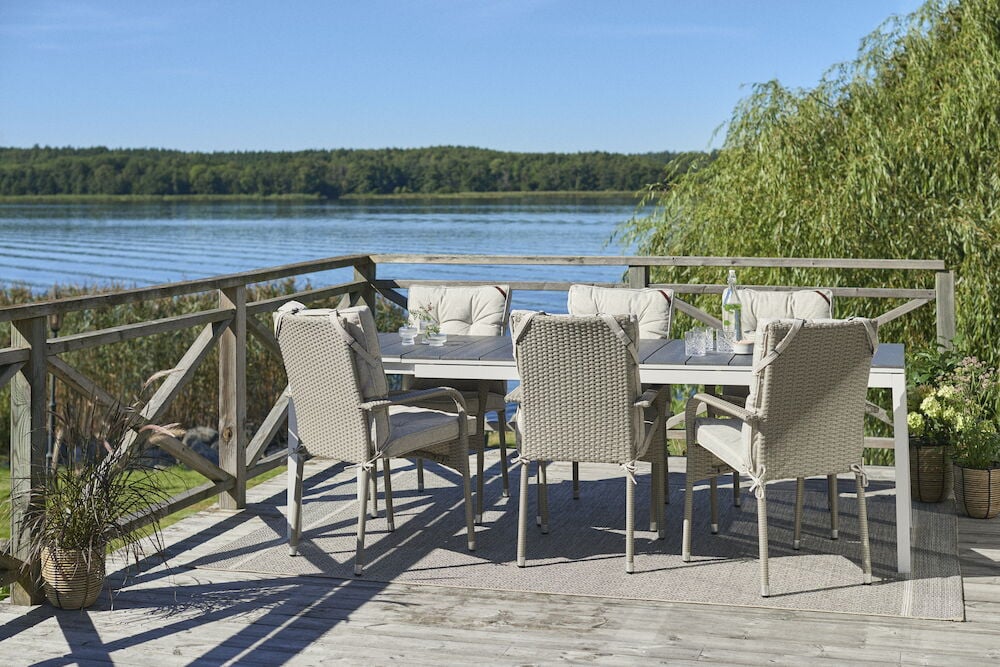 Kuusi vaaleanharmaata tyynyä ulkoruokapöydän tuoleilla.