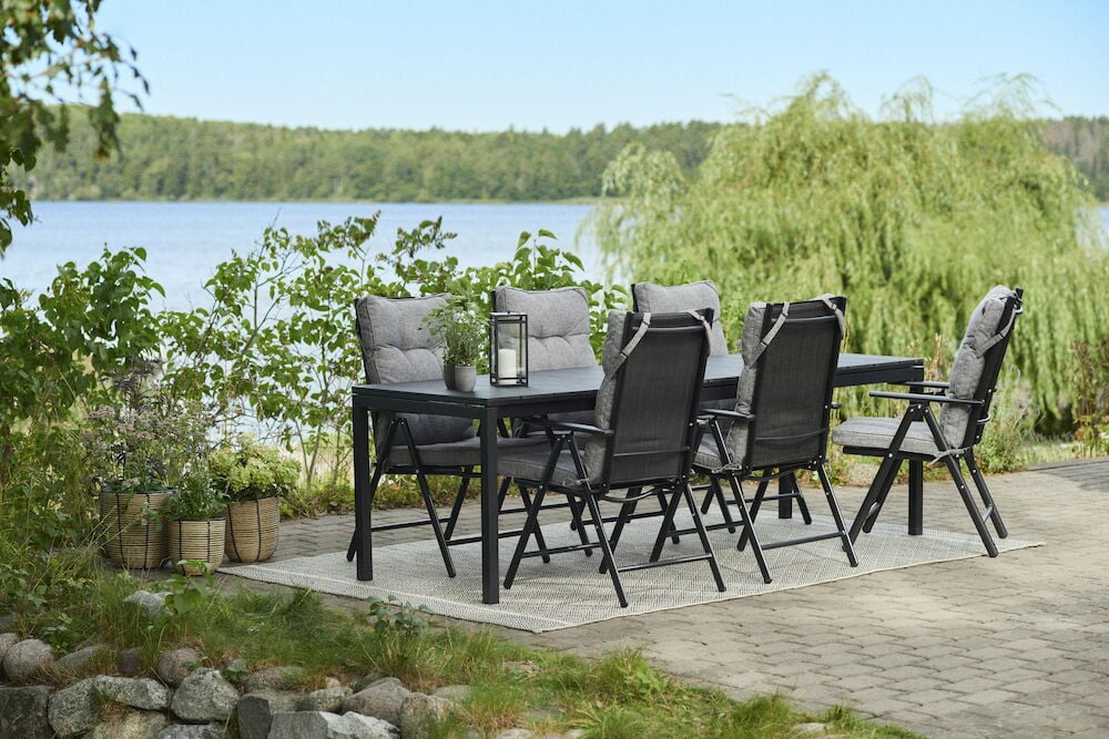 Harmaat tyynyt mustissa ulkotuoleissa pöydän ääressä ulkona.