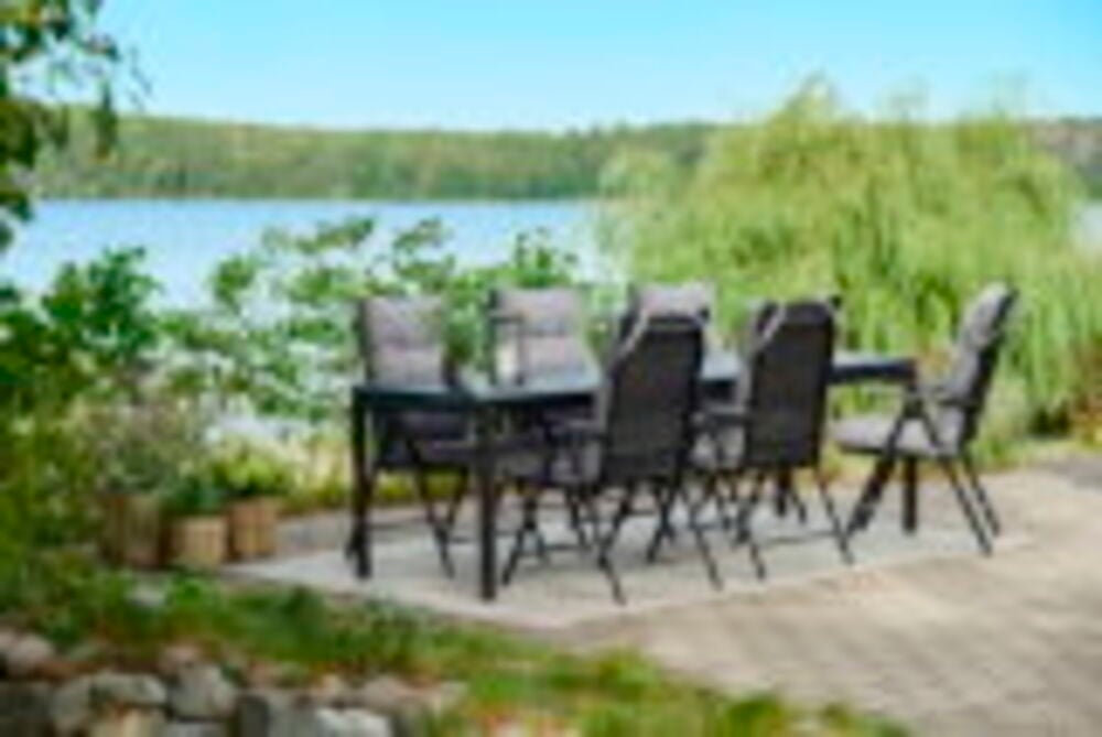 Kuusi mustaa alumiinista valmistettua asentotuolia ruokapöydän äärellä ulkona.