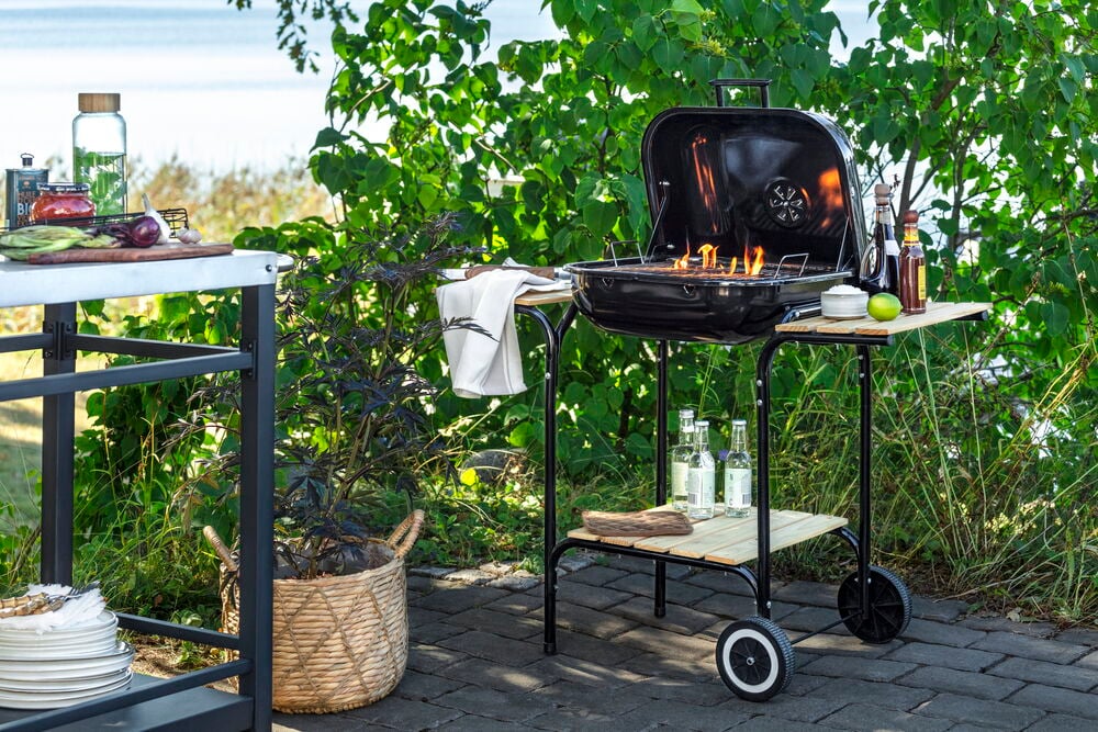 Svart kullgrill med trehyller utendørsmiljø.
