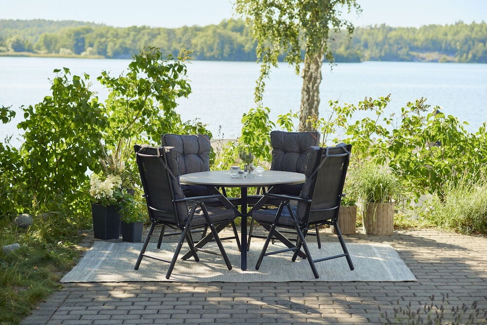 Pyöreä musta ulkopöytä, jossa neljä tuolia matolla.