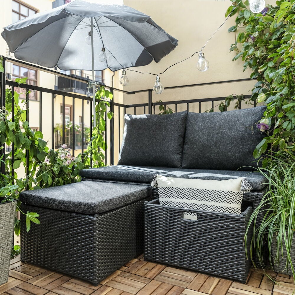 Musta oleskelusohva vihreällä parvekkeella tyynyineen.