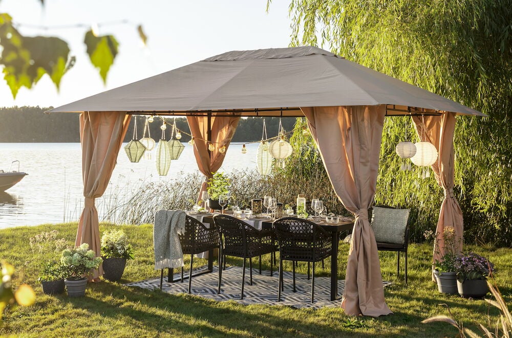 Stor beige paviljong med gardiner og utemøbler.