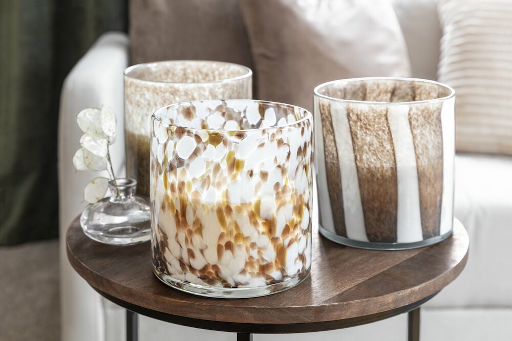 Drei braune und weiße Glas-Kerzenhalter auf Holztisch.