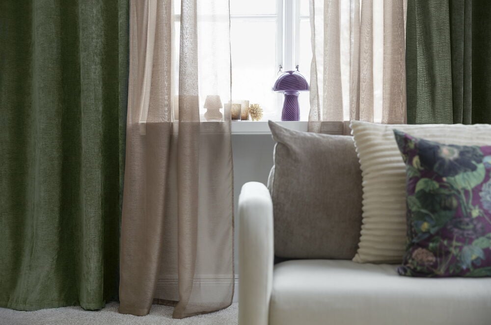 Tummanvihreät samettiverhot purjerenkailla ikkunassa.