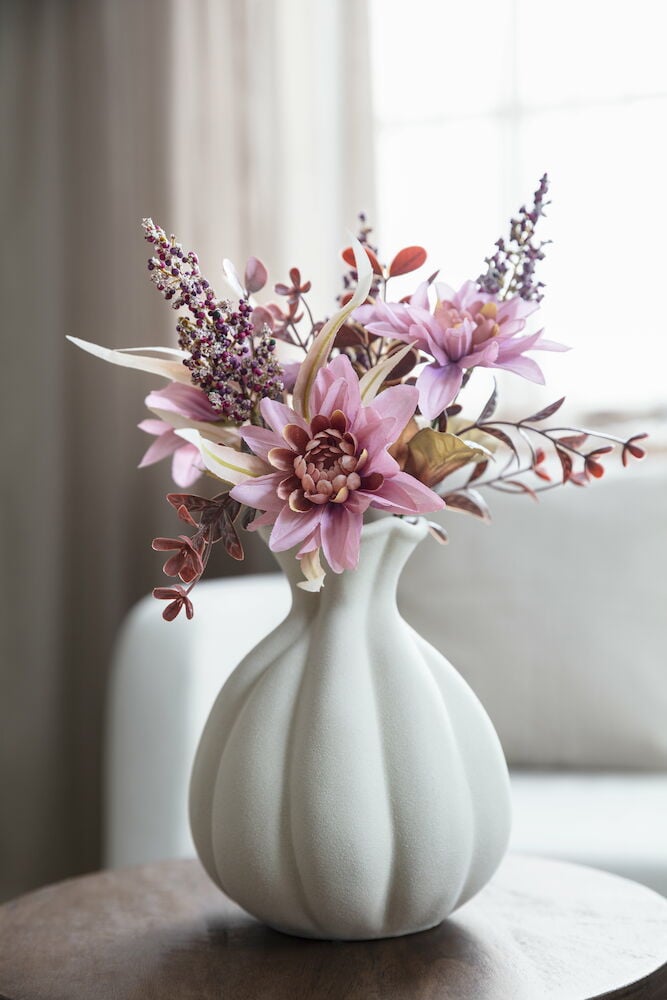 Beige kivitavaravaasi, jossa on vaaleanpunaisia kukkia.