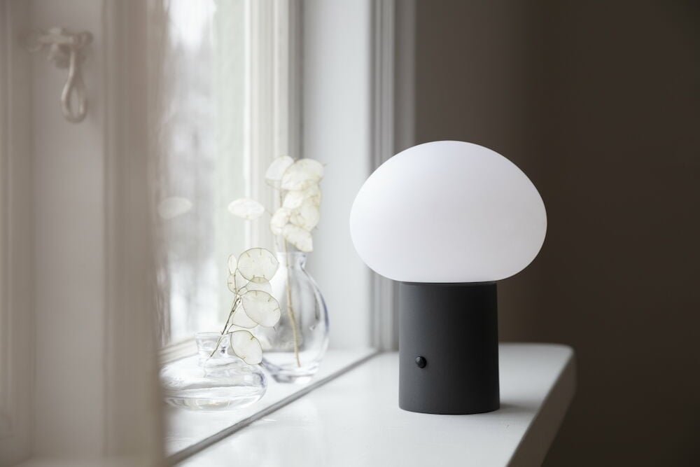 Moderni musta pöytälamppu, jossa on valkoinen kupu ikkunalaudalla.