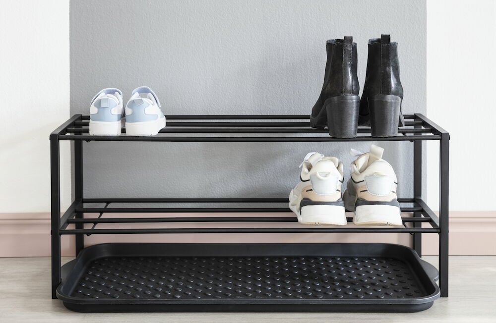 Musta kenkähylly, jossa on kolme paria kenkiä eteisessä.