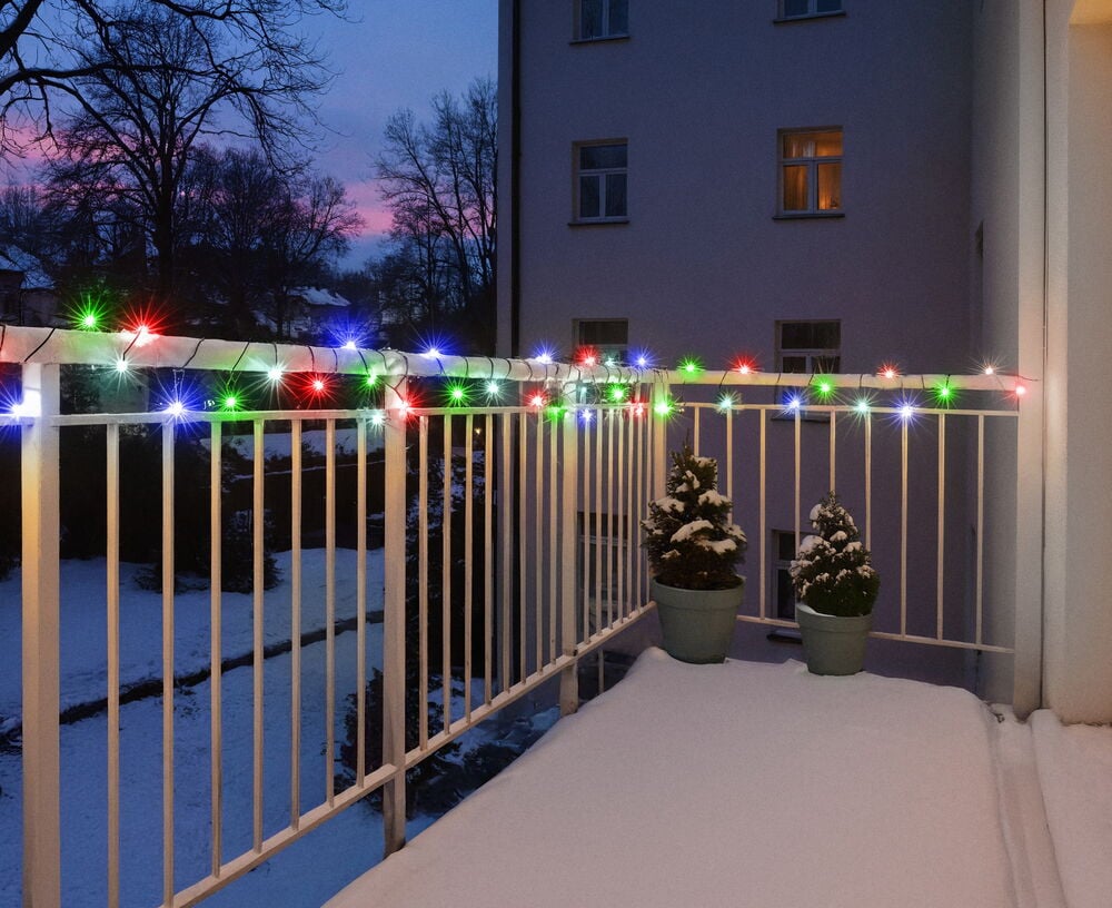 Lysslynge Glänsa 10 m, 81 LED Flerfarget drapert på et snødekket balkongrekkverk med potteplanter.
