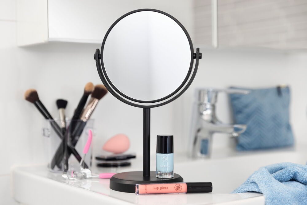 Läppglans och spegel på badrumshylla med sminkborstar.