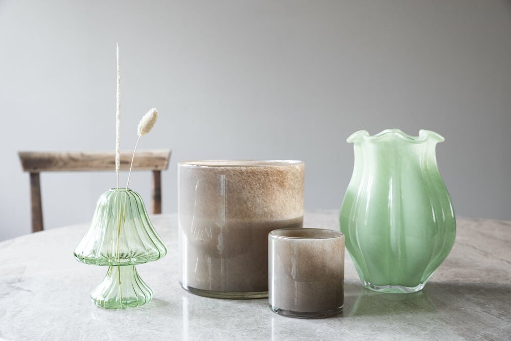 Grüne Glasvase mit welligem Rand auf Steinplatte.