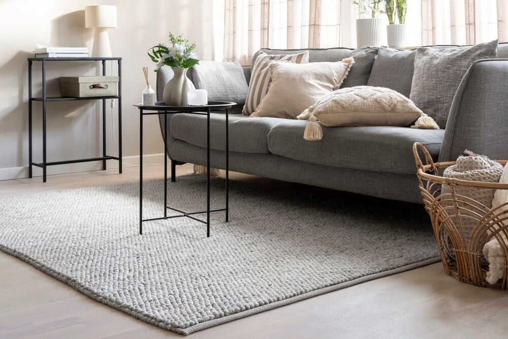 Et lys grått rektangulært teppe i ullblanding med teksturert overflate vises på et lyst tregulv.