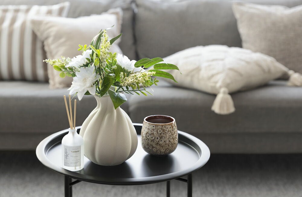 Beige stengodsvas med blommor på svart bord.