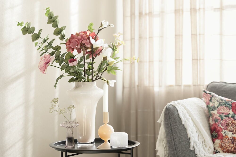 Iso vaaleanpunainen lasimaljakko kukilla mustalla pöydällä.