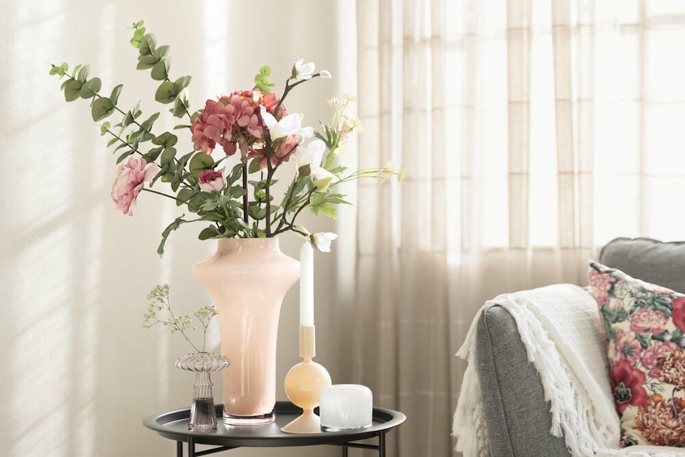 Ruusunvärinen lasivaasi mustalla sivupöydällä.