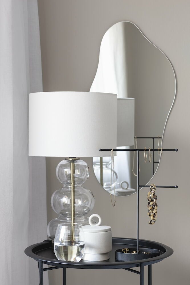 Organiskt formad spegel ovanför bord med lampa.
