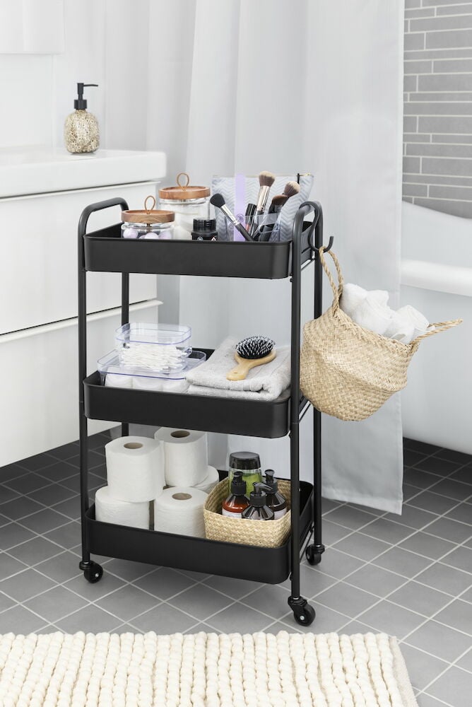 Svart rullvagn med tre hyllor i badrum.