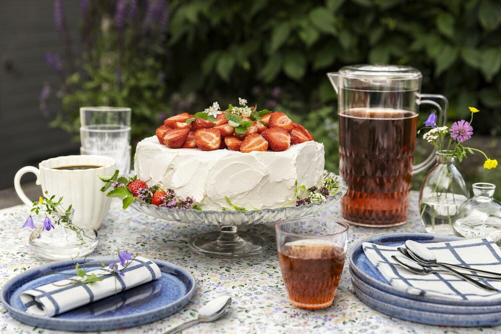 Muovikannu, jossa on juomaa, lasin ja kakun vieressä.