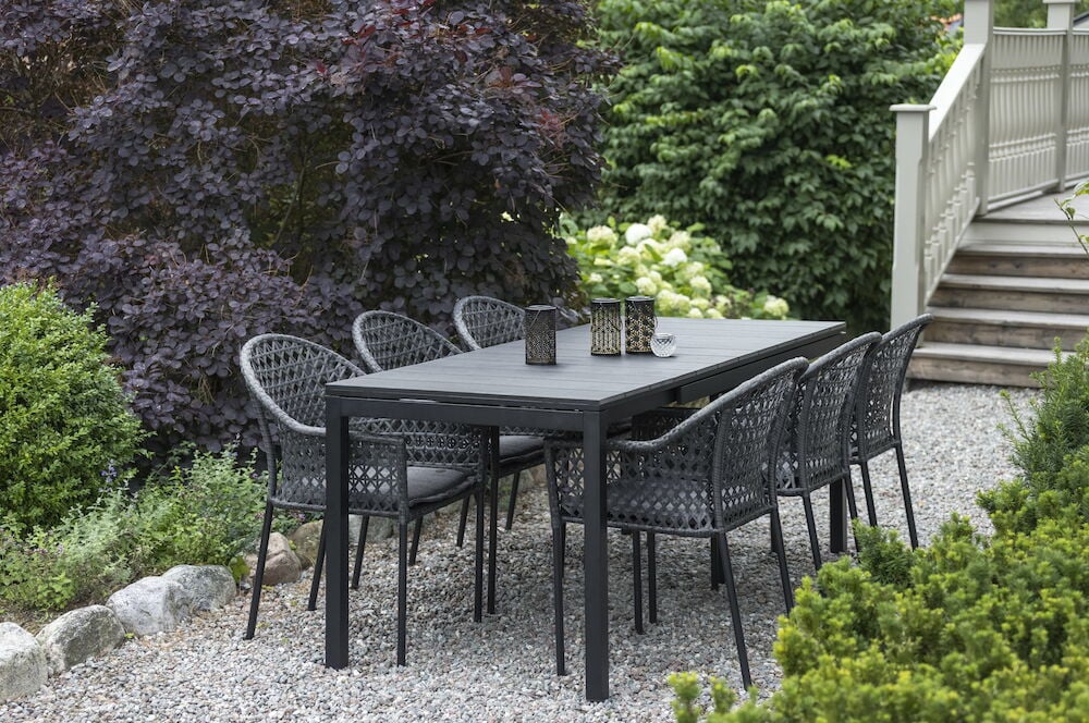 Kuusi mustaa polyrottinkituolia mustan ulkoruokapöydän ympärillä.