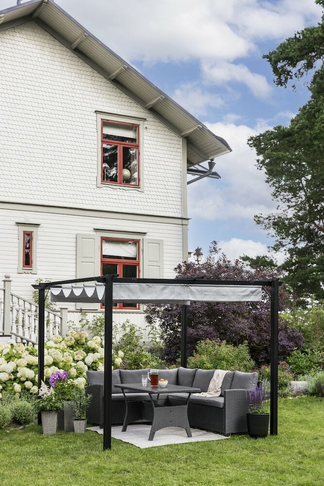 Svart pergola med tygtak i trädgård vid hus.