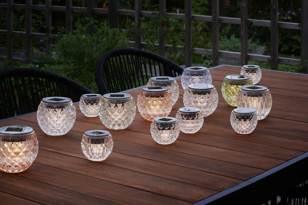 Mehrere Solarleuchten mit warmem Schein auf einem Holztisch im Freien.