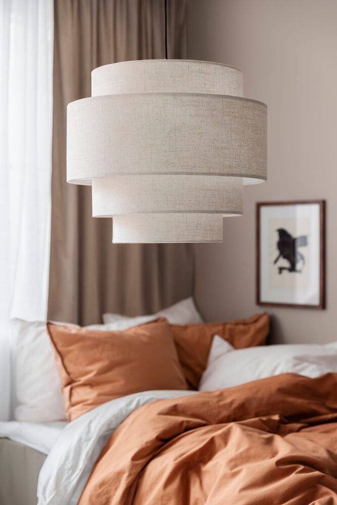 Hvit taklampe i lin over oppredd seng.