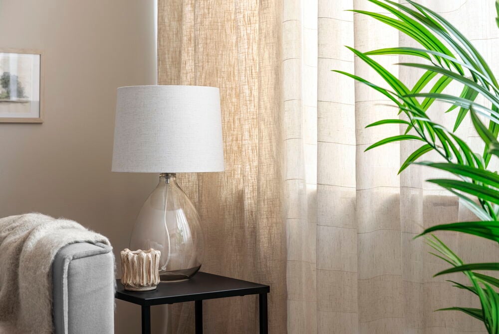 Bordslampa med glasfot och linneskärm på sidobord.