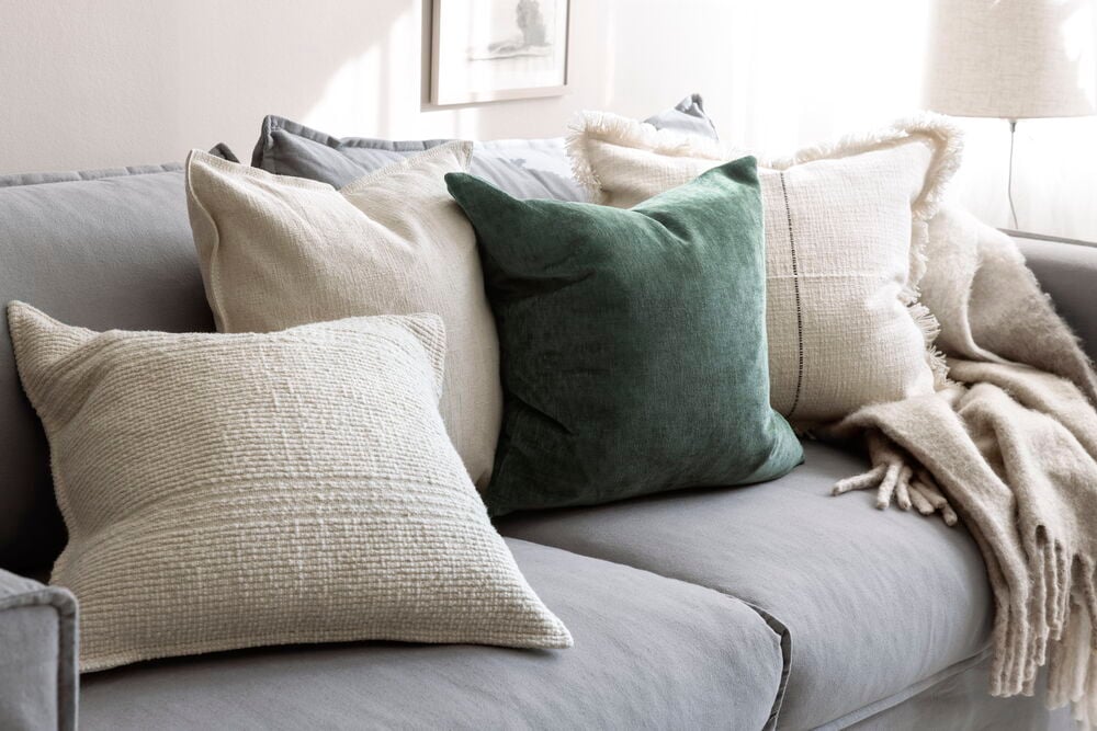 Mörkgrönt kuddfodral i sammet på ljus soffa.