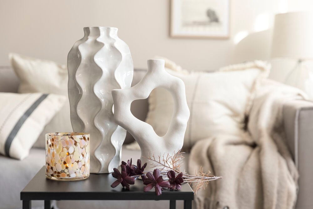 Valkoinen korkea vaasi, jossa on aaltomainen rakenne pöydällä.